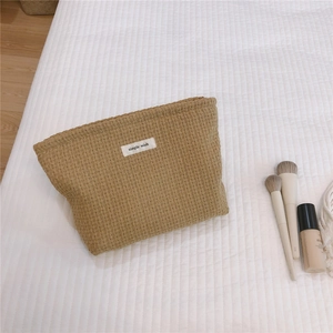 Detail of khaki waffle weave toiletry bag with zipper and simple wish label on bed