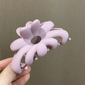 Detalle de una pinza de pelo con flor lavanda mate sostenida sobre un fondo gris