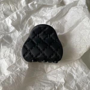 Detail of a black quilted matte claw clip with diamond pattern stitching on white paper