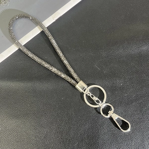 Detail of luxury rhinestone phone strap with silver ring and lobster clasp on black texture