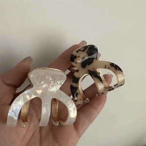 Detail view of pearl white and tortoiseshell acetate hair claws with gold-tone metal teeth