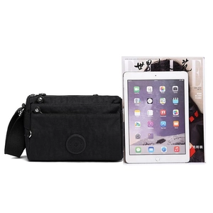 Black nylon crossbody bag with multiple pockets shown next to a tablet for size reference