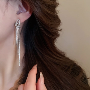 Close-up of silver knot heart earrings with long sparkling tassel on a model