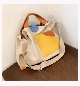 Detail of color-block canvas tote bag featuring yellow pocket and brown leather straps
