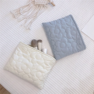 Detail of quilted floral embroidery on soft padded puffer cosmetic bags in cream and blue
