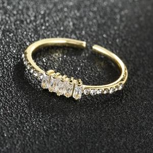 Bague ajustable dorée minimaliste avec cristaux taille baguette sur un fond noir texturé