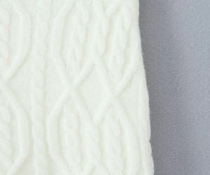 Close-up detail of white cable knit fabric showing soft texture and premium wool material