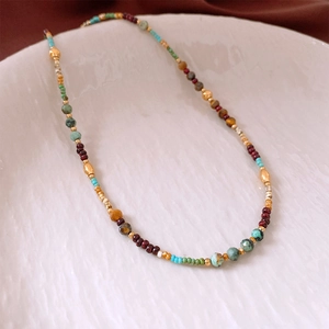 Detail of bohemian beaded necklace with turquoise and red stones on white ceramic plate