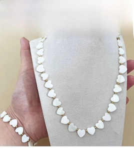 Detail view of heart-shaped shell beads necklace and bracelet set with golden steel accents