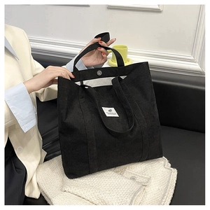 Close-up of black corduroy tote bag featuring a white label and magnetic closure detail
