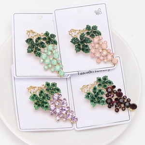 Detailed view of four colorful rhinestone grape brooches on gold metal bases in a white tray