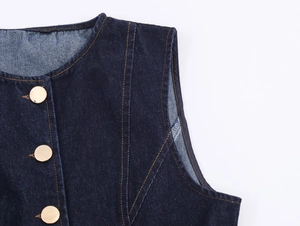 Détail du gilet en jean bleu foncé avec boutons dorés et surpiqûres jaunes contrastées