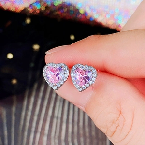 Macro shot of heart-shaped pink zircon earrings with silver halo on a finger