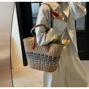 Detail of straw tote bag with blue wave pattern and brown PU leather handles