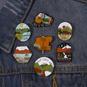 Collection of outdoor camping enamel pins featuring mountain landscape designs on denim jacket