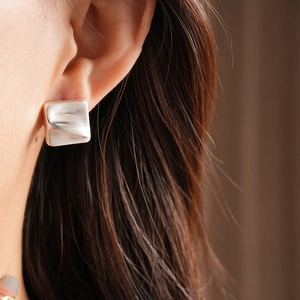 Macro shot of square silver earrings with a unique rippled texture on female ear