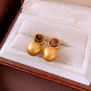 Close-up of golden leopard print square studs with matte ball pendants in a jewelry box