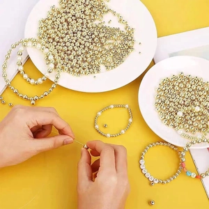 Close-up of hands crafting DIY jewelry using gold spacer beads and alphabet pearls