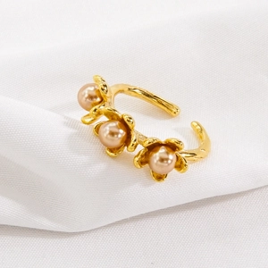 Elegant gold flower ring with peach pearls and adjustable band on soft white fabric