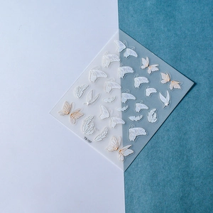Vue macro de stickers d'ongles papillons 3D avec reliefs dorés et détails d'ailes blanches