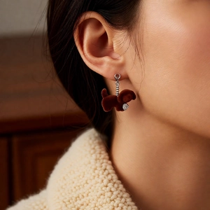 Close-up of a brown flocked puppy pendant earring worn by a model in a warm setting