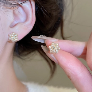 Close-up of elegant flower stud earrings with pearls and rhinestones on model ear