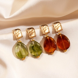 Metallic square studs with green and amber acrylic teardrop pendants on silk backdrop