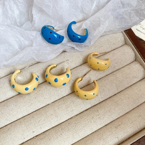 Detailed view of enamel spotted C-shaped earrings in blue and yellow within a jewelry box