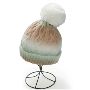 Close-up of ombre cable knit beanie with fluffy faux fur pompom on metal stand
