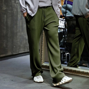 Detail of olive green pleated pants showing elastic drawstring waist and textured fabric