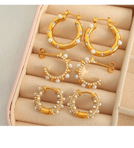 Macro detail of three gold C-shaped earrings with pearls and crystals in a velvet tray