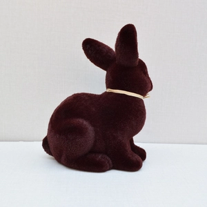 Detail shot of a sitting dark brown flocked Easter rabbit with a cream ribbon bow