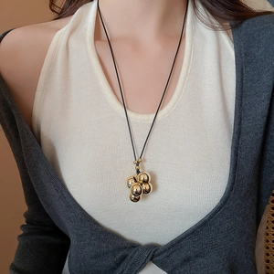 Dettaglio di una collana con ciondolo a sfere dorate geometriche su un cordino nero chic