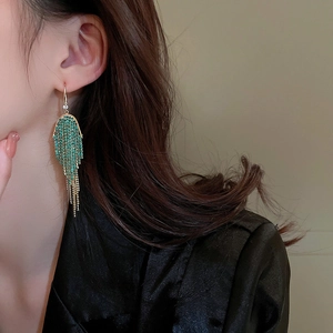 Detail of long tassel earrings with green rhinestones and gold chains on model