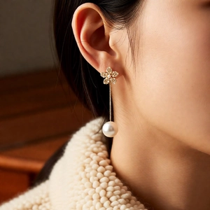 Detailed shot of 18k gold flower earrings with white pearls on a model wearing a sweater