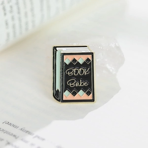 Book-shaped enamel pin with BOOK Babe text on a crystal and book page background