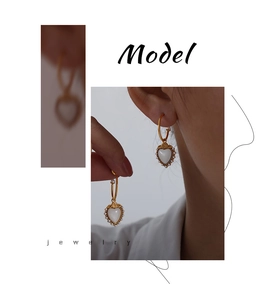 Close-up of gold heart earrings with white mother-of-pearl inlay and floral accents