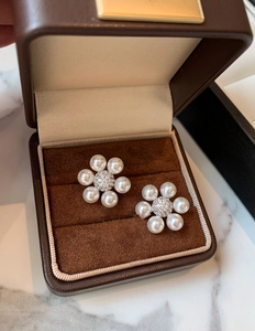 Gros plan de boucles d'oreilles fleur en perles et zircon dans un écrin marron