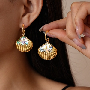 Detailed view of gold-tone seashell earrings with iridescent mother-of-pearl inlay on model