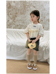 Vertical full-body view of a girl in cream mock-layered top and denim shorts with yellow bag