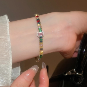 Primo piano di un braccialetto d'oro con zirconi rettangolari colorati sul polso di una donna