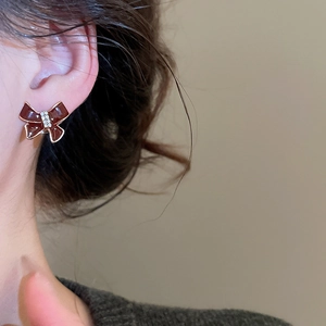 Close-up of a deep red enamel bow stud earring with diamonds worn by a model