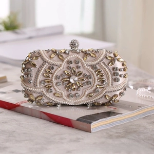Detailed view of champagne satin evening clutch with intricate pearls and crystal accents