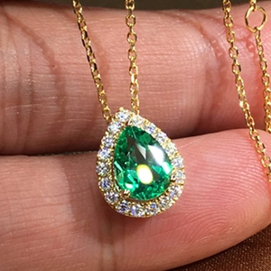 Close-up of a pear-cut emerald green zircon pendant with a gold halo and chain