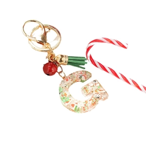 Christmas letter G keychain with snowman tree charms, red bell and green tassel on gray background