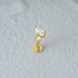 Macro view of golden labret piercing featuring pear and round cut clear gemstones