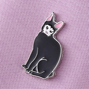 Macro shot of an enamel black cat pin with pink ears on a soft pink fabric background