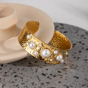 Macro detail of hammered gold cuff bracelet with pearl inlay against stone background