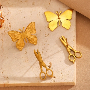 Vue détaillée des boucles d'oreilles dorées papillon et ciseaux sur un socle en pierre