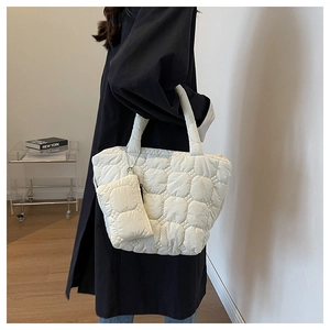 Close-up of white quilted tote bag with mini zip pouch on a black coat background